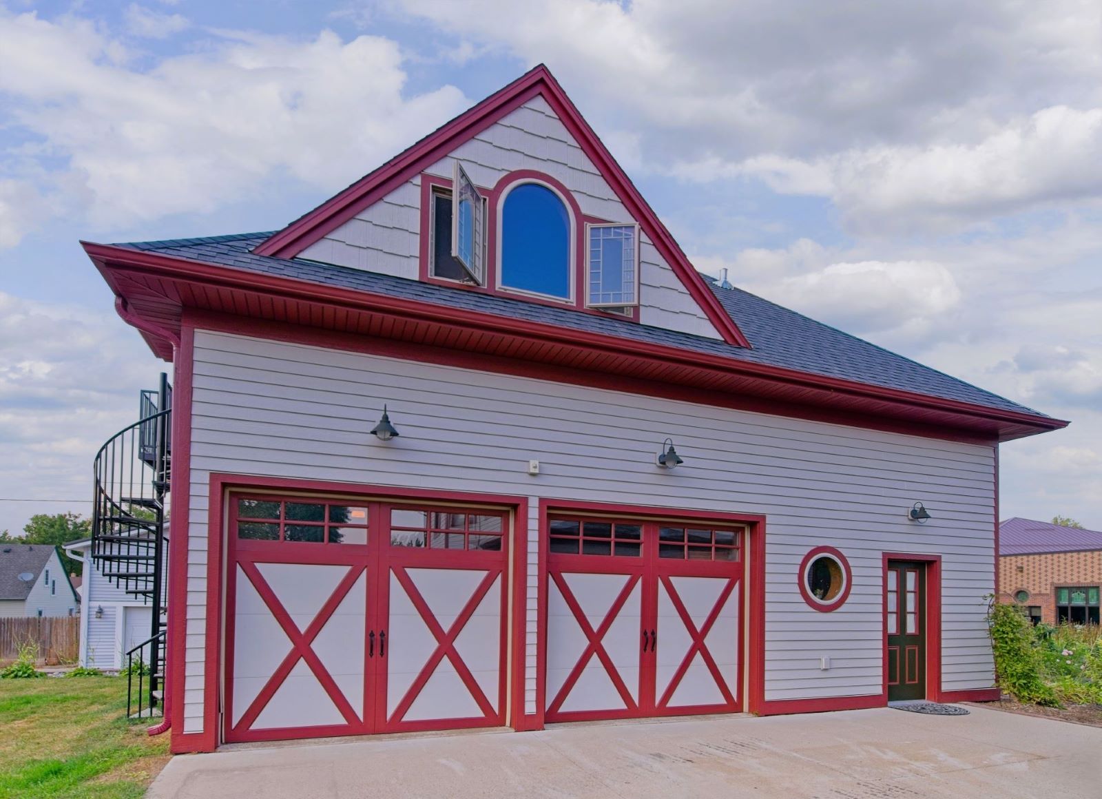 Two-story carriage house garage matching the historic 1899 home at 504 W. Cavour Ave in Fergus Falls, Minnesota, with fresh light gray siding, deep red trim, and carriage-style doors by Big Boys Painting.