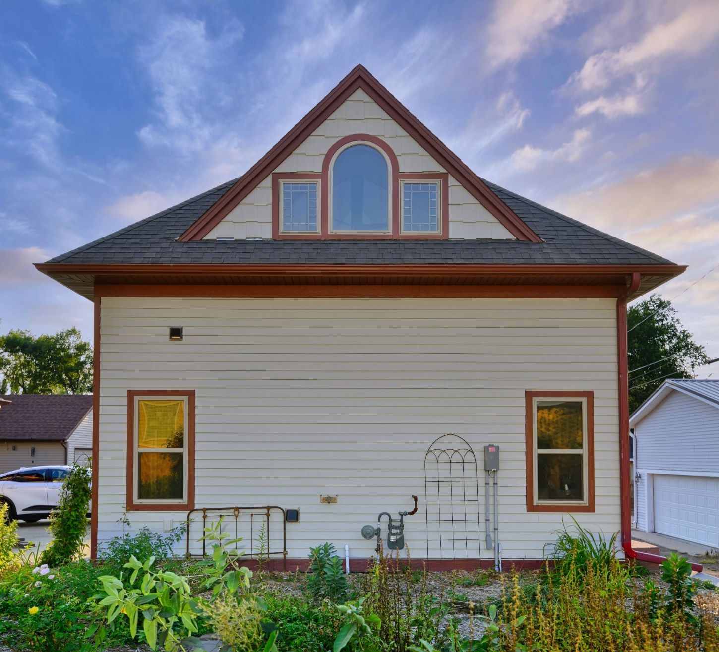 East facade of the detached two-story carriage house at 504 W. Cavour Ave in Fergus Falls, Minnesota, showcasing matching light gray siding, red trim, and a grand upper window peak.