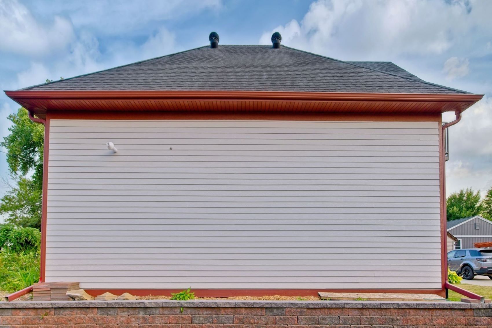 Straight-on rear view of the detached carriage house at 504 W. Cavour Ave in Fergus Falls, Minnesota, highlighting the flat gray lap siding, clean red trim lines, and a brick retaining wall.