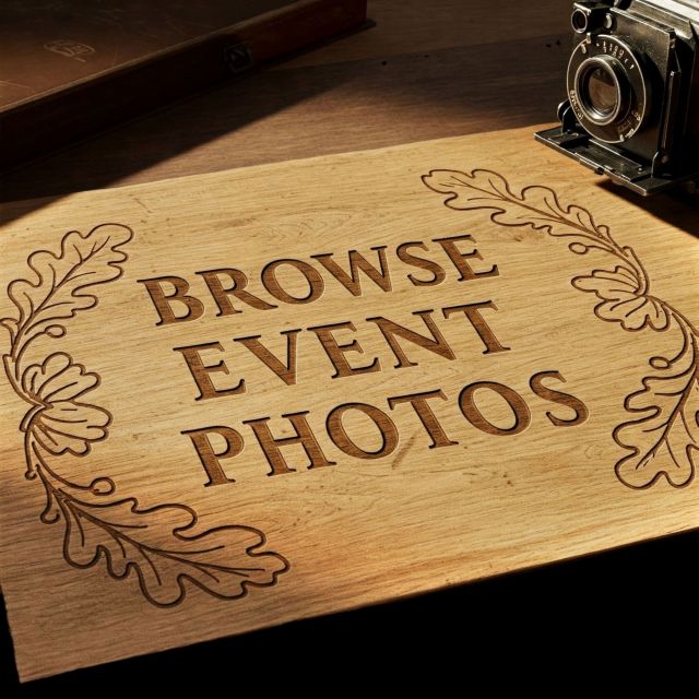 An engraved wooden sign reading "BROWSE EVENT PHOTOS" in bold capital letters, flanked by chiseled oak leaf branches on a rustic desk next to a vintage camera.