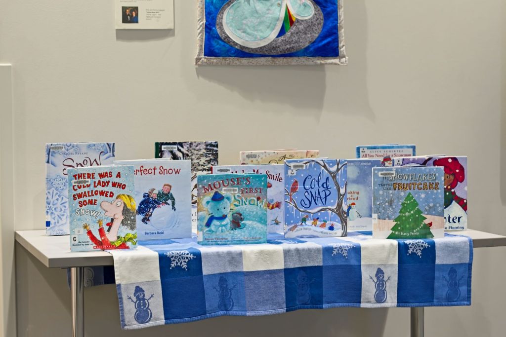 A library display table featuring a collection of winter-themed children's picture books arranged on a blue and white snowflake runner.
