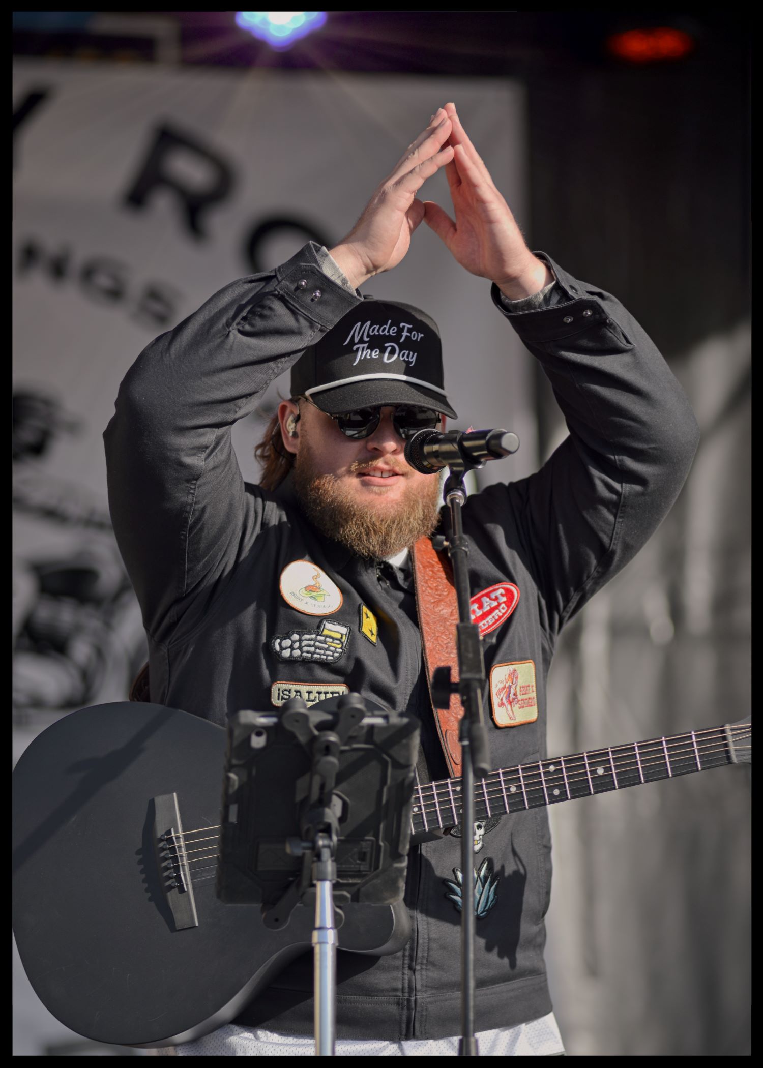 Musician Chris Tungseth raising both hands in a pyramid shape above his head while singing behind a microphone on stage in Fergus Falls, Minnesota.