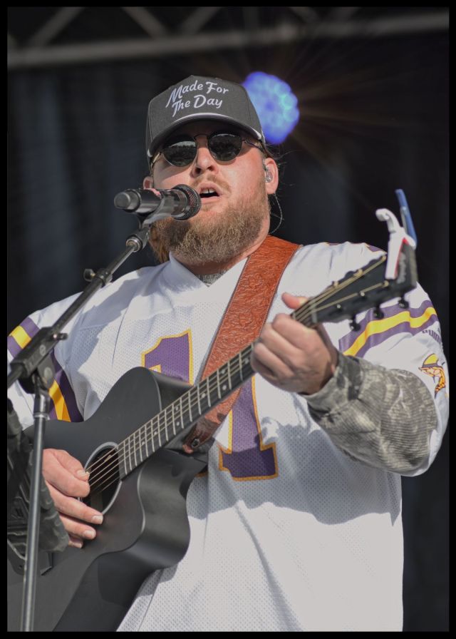 Country music artist Chris Tungseth singing and playing a black acoustic guitar on stage during a performance in Fergus Falls, Minnesota.