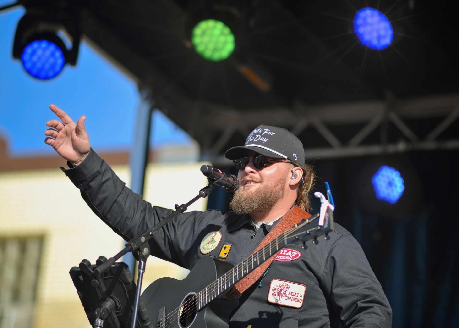 Musician Chris Tungseth raising his arm toward the crowd while singing and playing a black acoustic guitar on stage in Fergus Falls, Minnesota.
