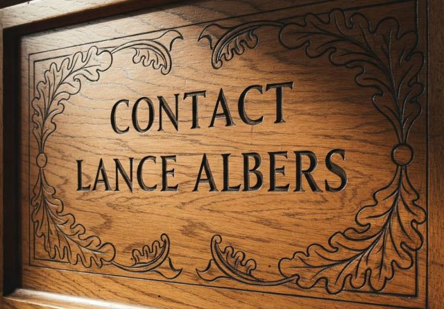 Carved wooden sign with the text "Contact Lance Albers" framed by ornate leaf engravings, used as a website contact link for fine art, commercial photography, and portrait services based in Fergus Falls, MN.