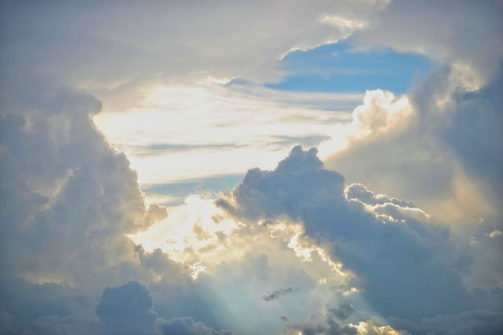 Bright sunbeams breaking through a wide opening in heavy storm clouds under a patch of blue sky.