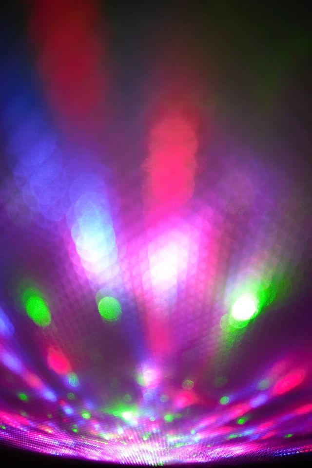 An abstract highly creative photograph of vibrant pink, magenta, green, and blue bokeh light leaks casting upward rays over a textured mesh surface.
