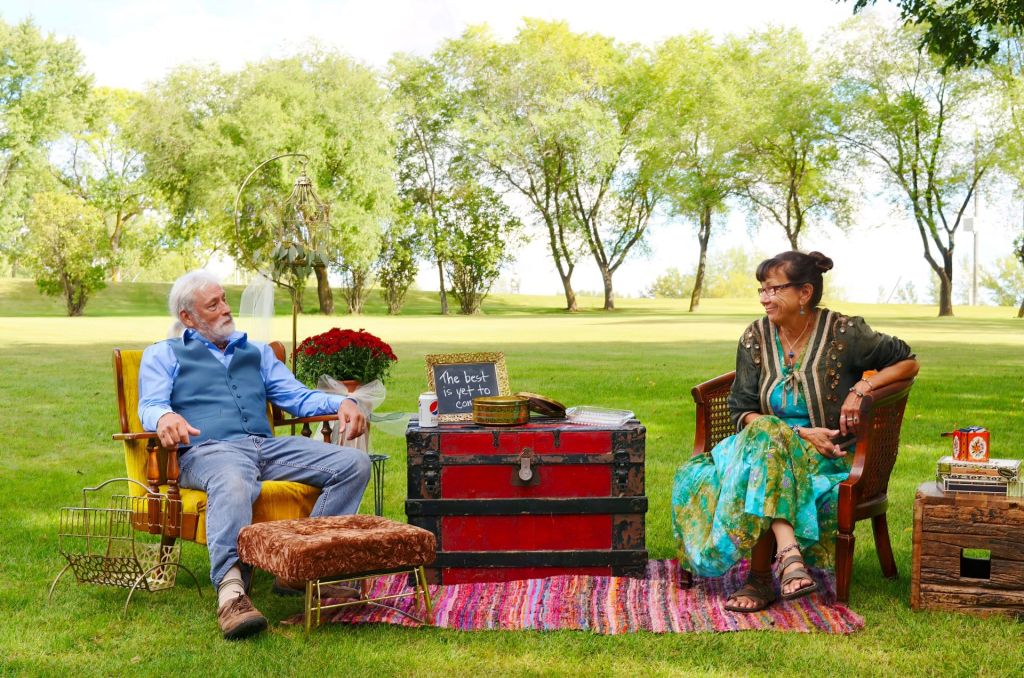 A couple sitting in vintage armchairs during an outdoor stylized portrait session in a green park, photographed by Lance Albers.