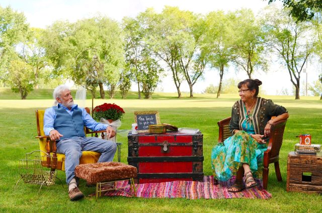 A couple sitting in vintage armchairs during an outdoor stylized portrait session in a green park, photographed by Lance Albers.