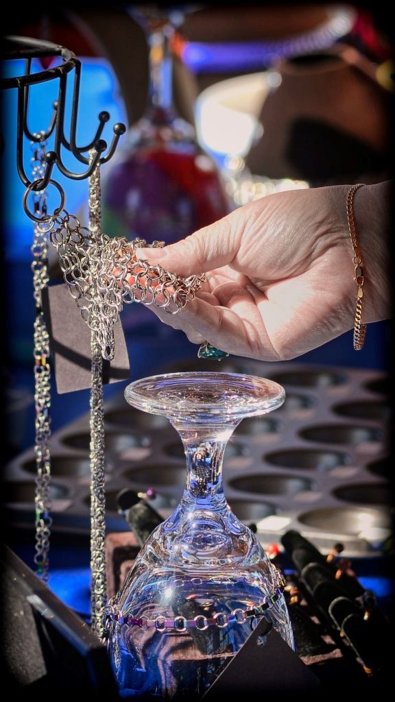 Close-up photograph of a customer's hand examining a handmade stainless steel chainmail necklace at the Steel Crazy artisan vendor booth.