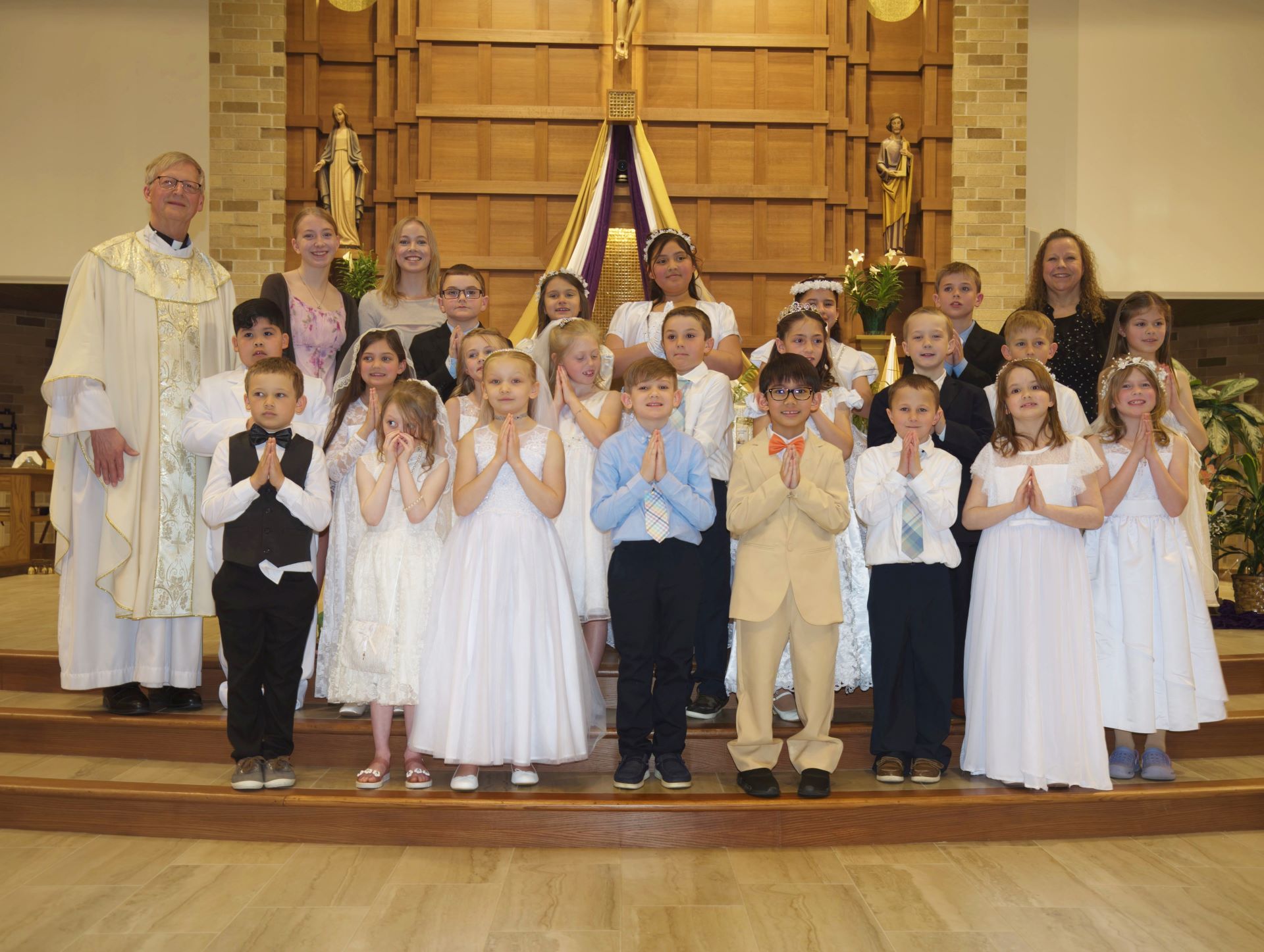 A group photograph of children, a priest, and catechists standing on the altar steps inside St. Anastasia Catholic Church in Hutchinson, MN, celebrating their First Holy Communion on April 30, 2023.