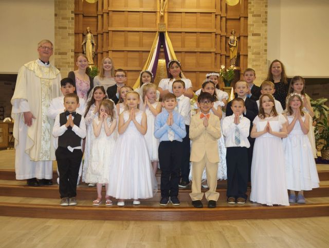 A group photograph of children, a priest, and catechists standing on the altar steps inside St. Anastasia Catholic Church in Hutchinson, MN, celebrating their First Holy Communion on April 30, 2023.