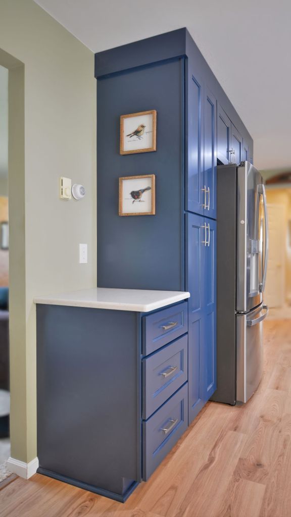 Modern kitchen featuring custom navy blue cabinets with gold T-bar handles, a quartz countertop, and a stainless steel French door refrigerator.