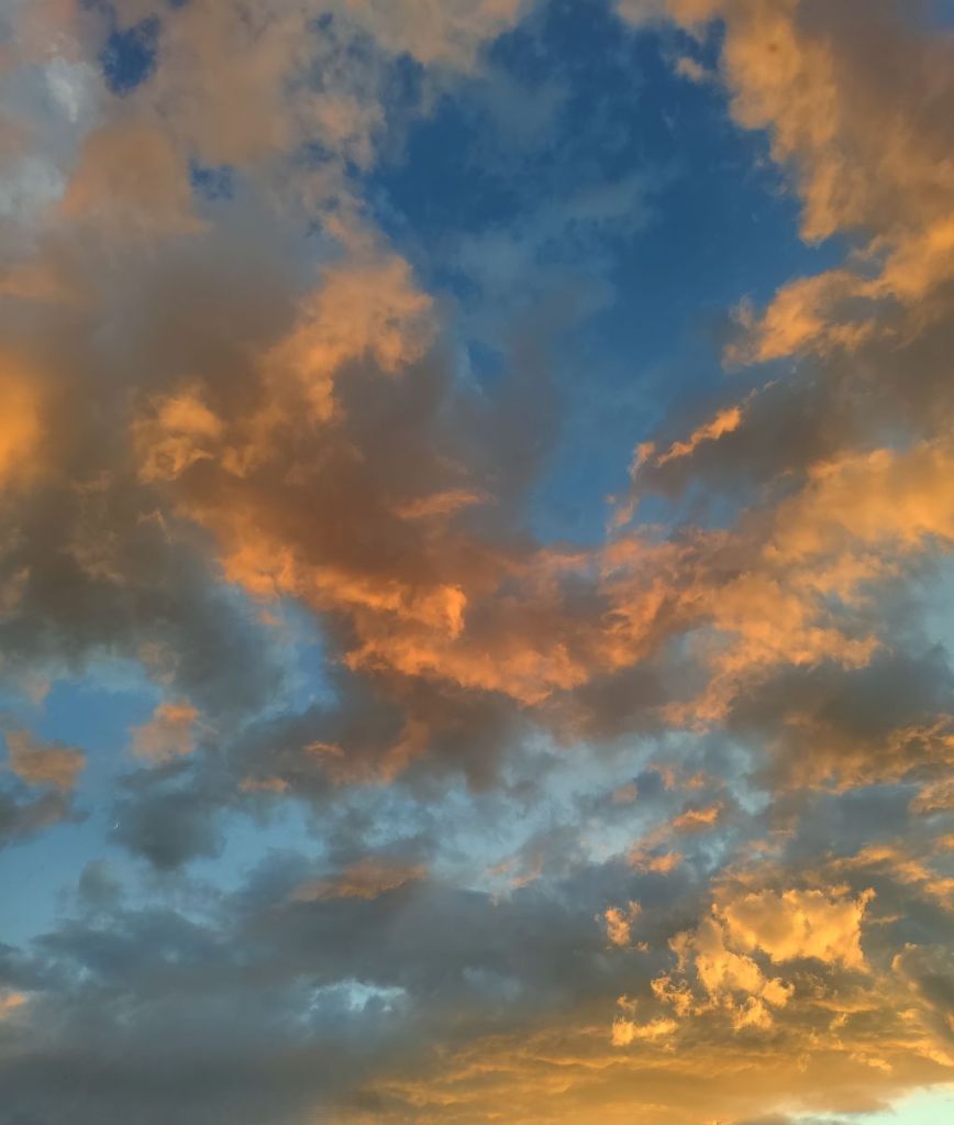 Dramatic sunset sky over Otter Tail County featuring scattered clouds illuminated in vibrant orange and golden hues against a deep blue sky background.