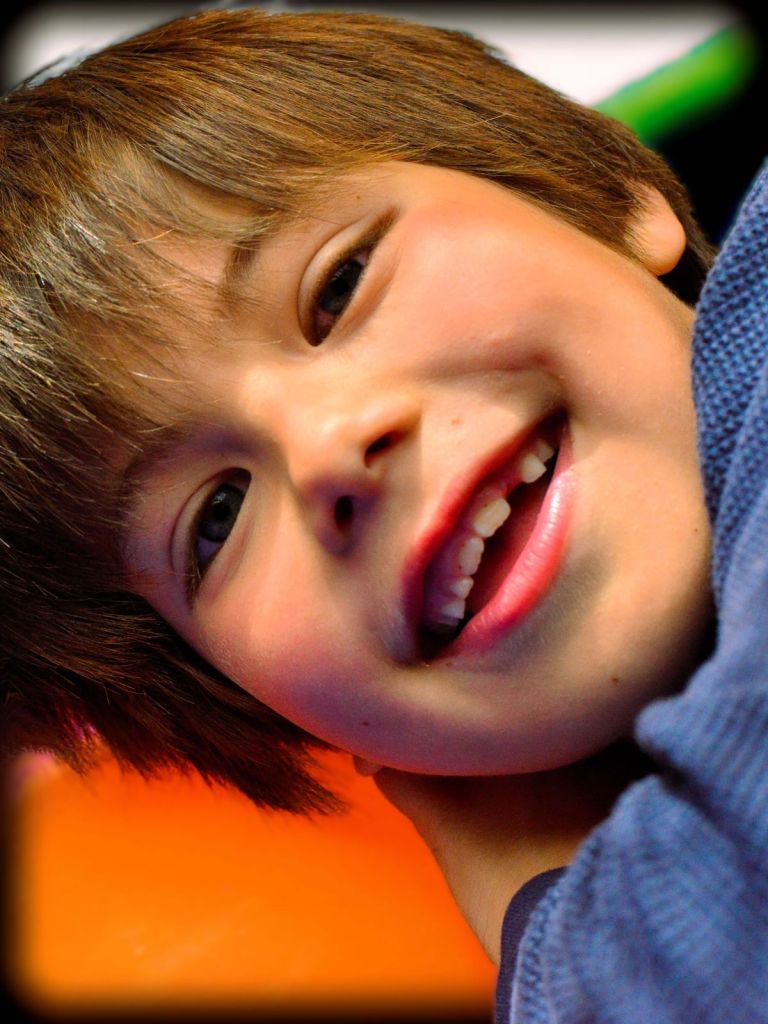 Close-up of a young boy smiling warmly while tilting his head.