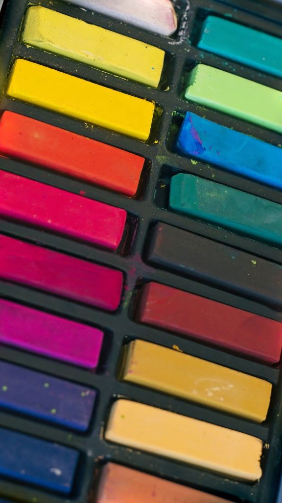 Vertical close-up view of an organized plastic tray filled with brightly colored rectangular chalk pastel sticks arranged in rows of yellow, red, pink, green, and blue.