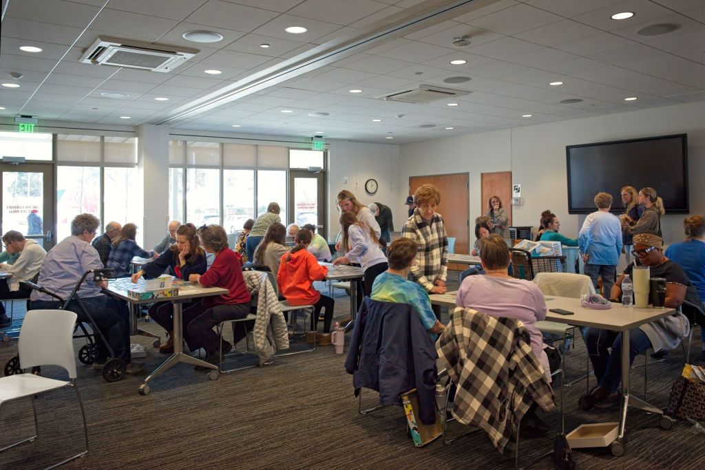 A wide-angle shot of a busy community jigsaw puzzle contest inside the community room at the Fergus Falls Public Library.