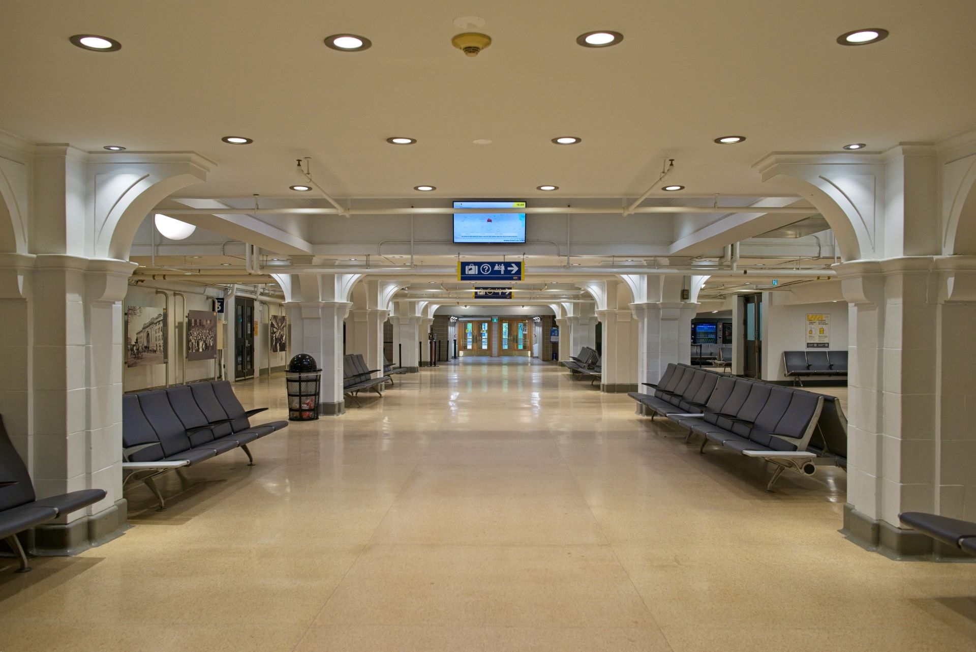 The spacious interior waiting area of Winnipeg Union Station, featuring rows of dark gray seating, white architectural pillars, and polished terrazzo flooring.
