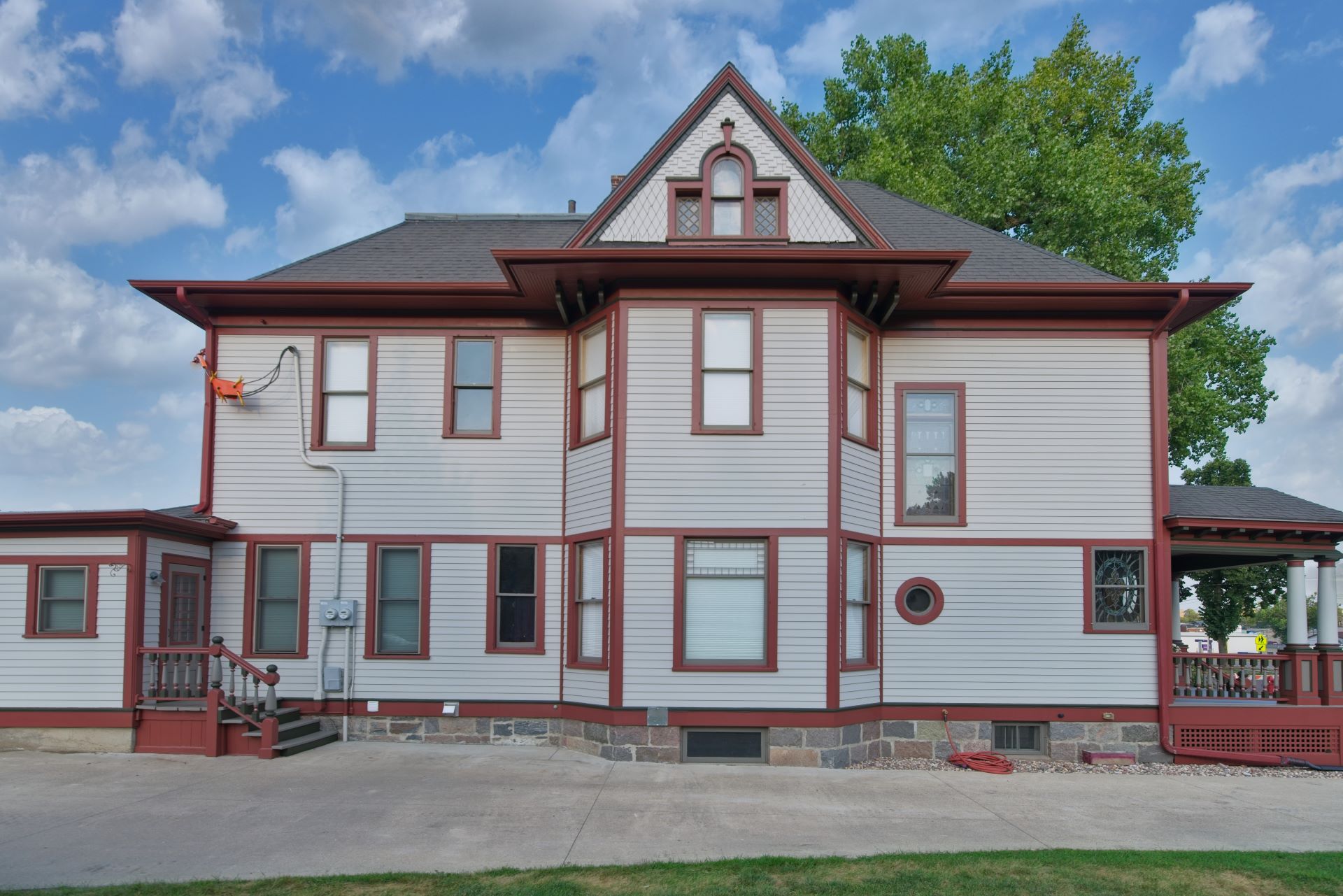 Side exterior view of a historic Victorian home in Fergus Falls, Minnesota, featuring light gray siding and deep red trim after a professional repainting.