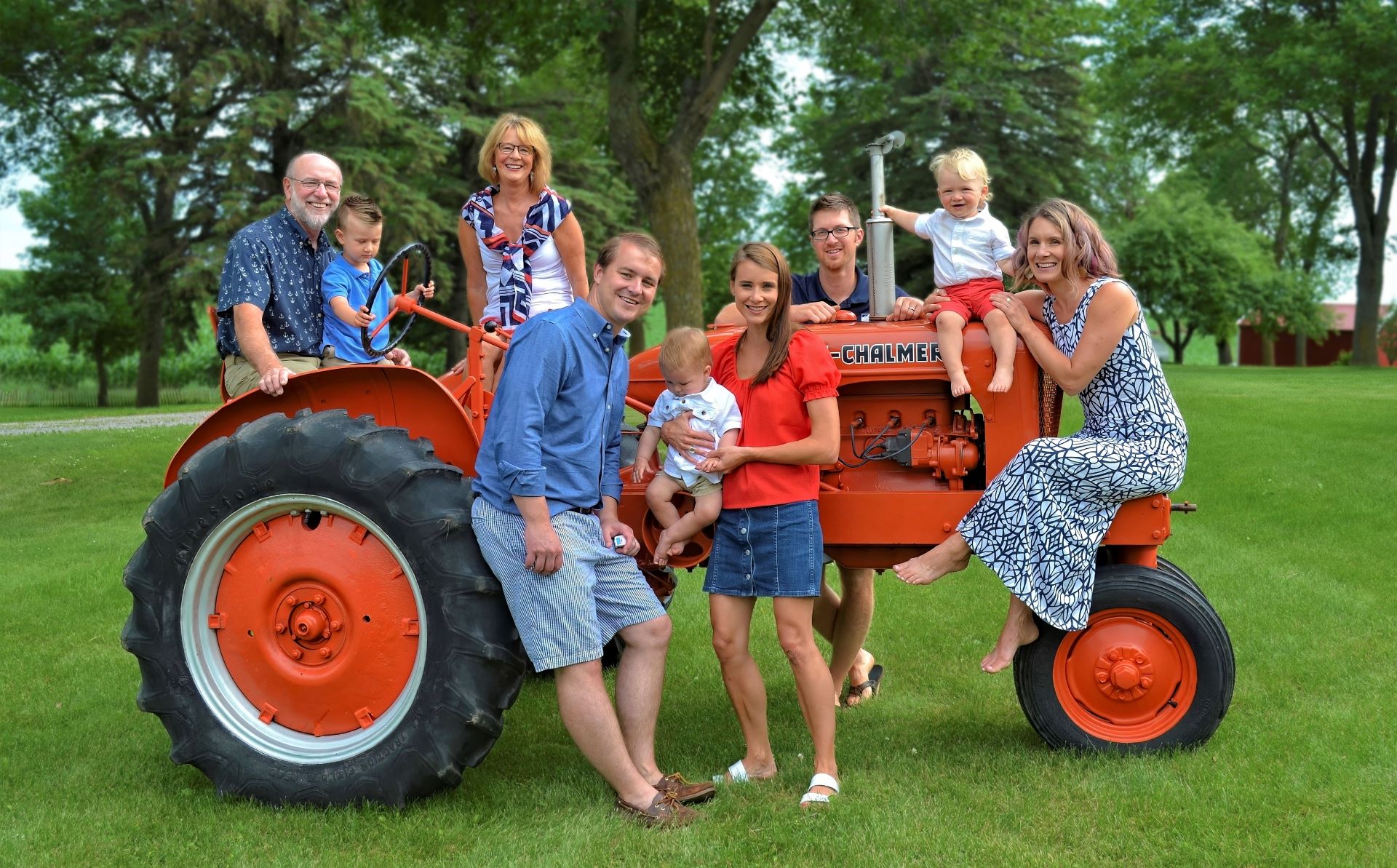 Multi-generational family posing together around a vintage orange Allis-Chalmers tractor on a green lawn.