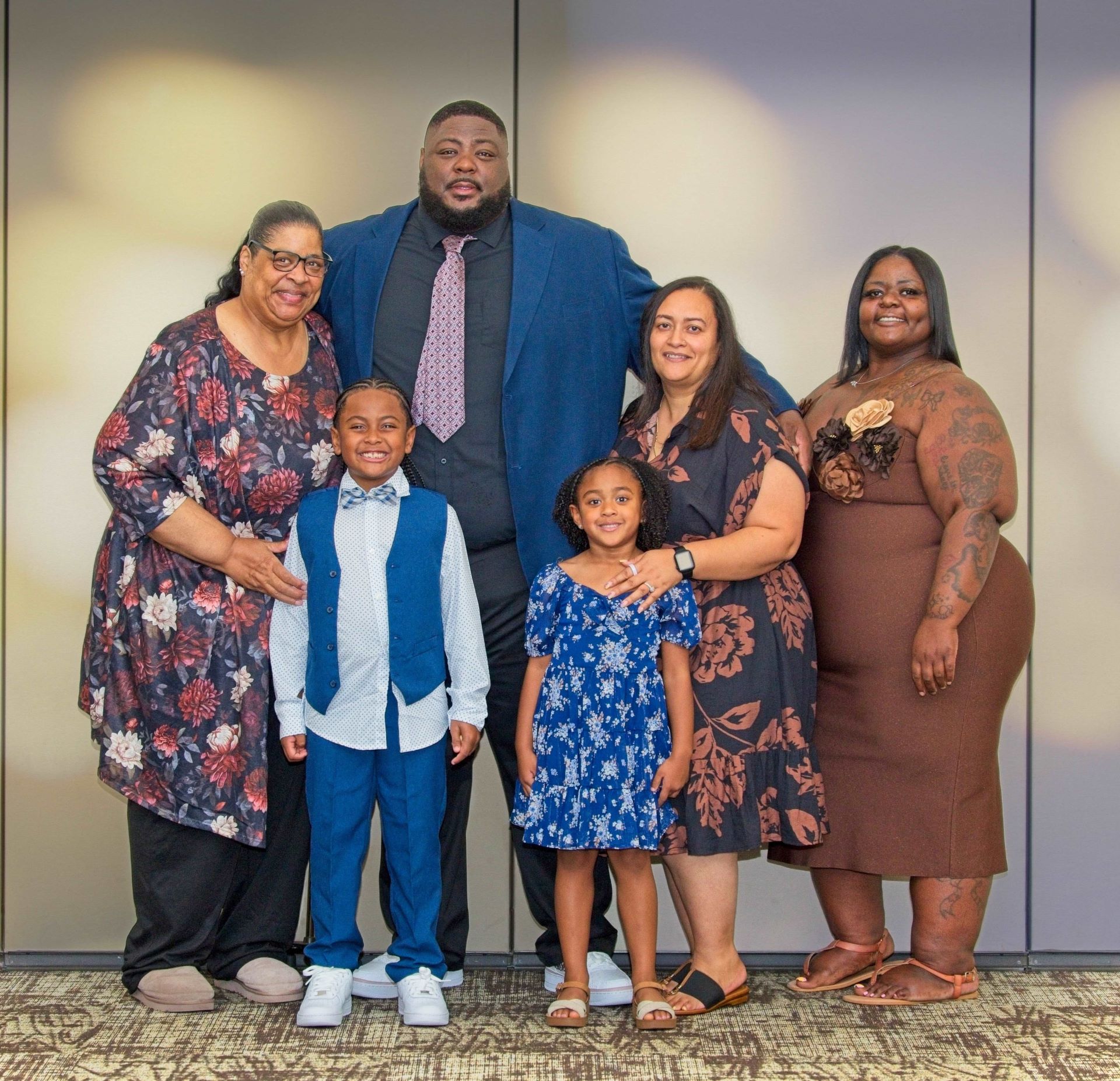 A formal indoor family group portrait featuring four adults and two young children dressed up for a special celebration.