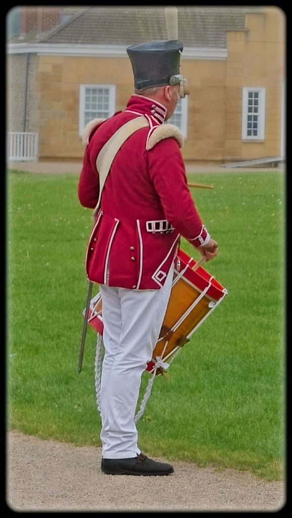 Rear profile or side profile photograph of a historic re-enactor dressed as a 19th-century military drummer in a red coat and white trousers at Historic Fort Snelling.