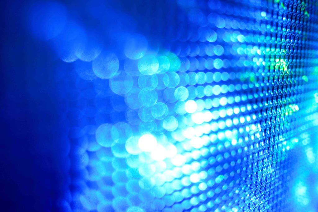 Abstract photograph of vibrant blue and teal bokeh lights casting a bright glow over a patterned mesh surface.