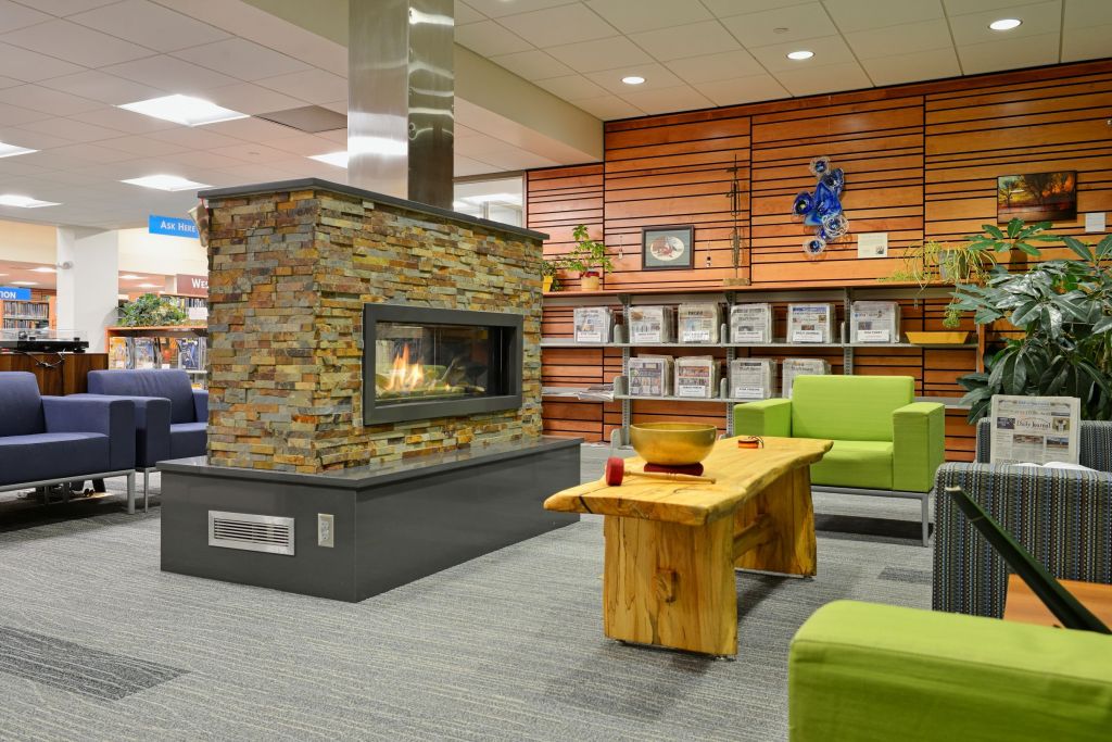 Modern stone fireplace lounge with lime green armchairs and a live edge wood coffee table at the Fergus Falls Public Library.
