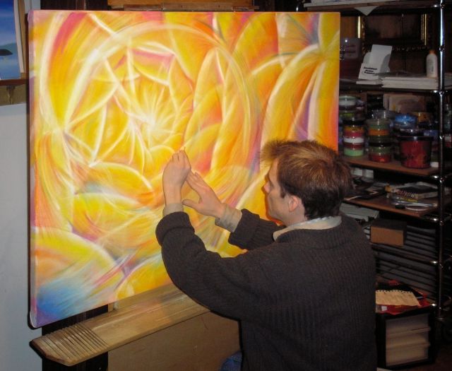 Fine artist Lance Albers applying vibrant yellow and orange chalk pastels to a large canvas on an easel, creating a glowing abstract spiral sunburst pattern.